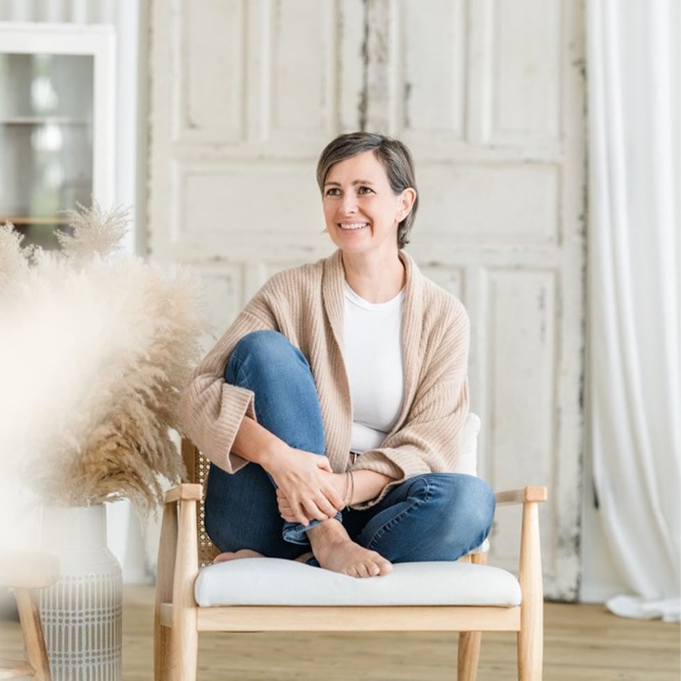 Donna sorridente seduta su una sedia in una stanza luminosa e moderna.