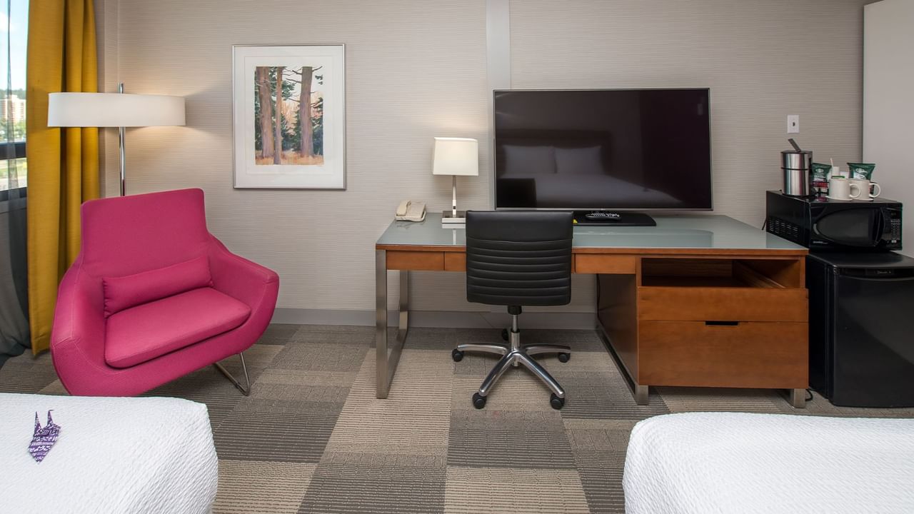 A hotel room with a desk, chair, TV, microwave, refrigerator, and two queen beds.