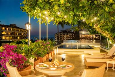 Dinner table with wine by rooftop pool and blooming pink bougainvillea under lit trees at Casa Dona Susana