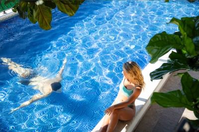 Woman sitting by the poolside edge while a man swimming completely underwater in a pool at Casa Dona Susana