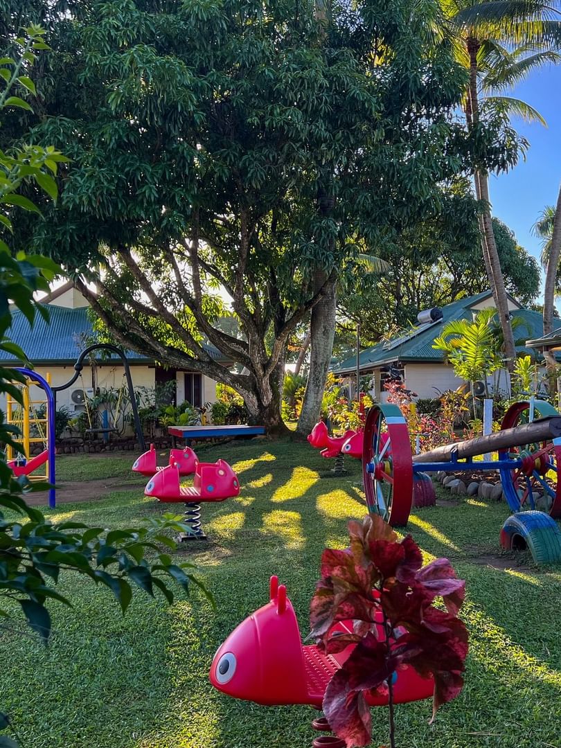 Kids play area with red rides by a see-saw under tropical palm trees at Tokatoka Resort - Fiji International Airport, Nadi