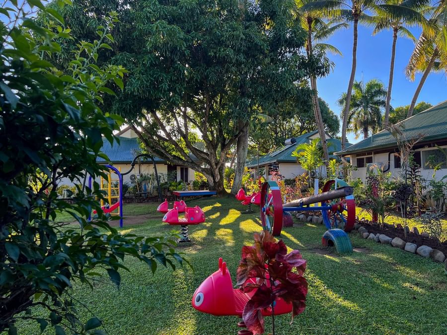 Kids play area with red rides by a see-saw under tropical palm trees at Tokatoka Resort - Fiji International Airport, Nadi