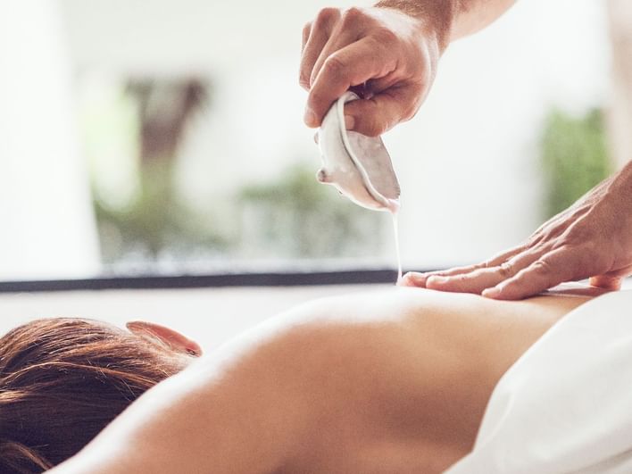 A person is applying oil to a woman lying on her stomach on a massage table.