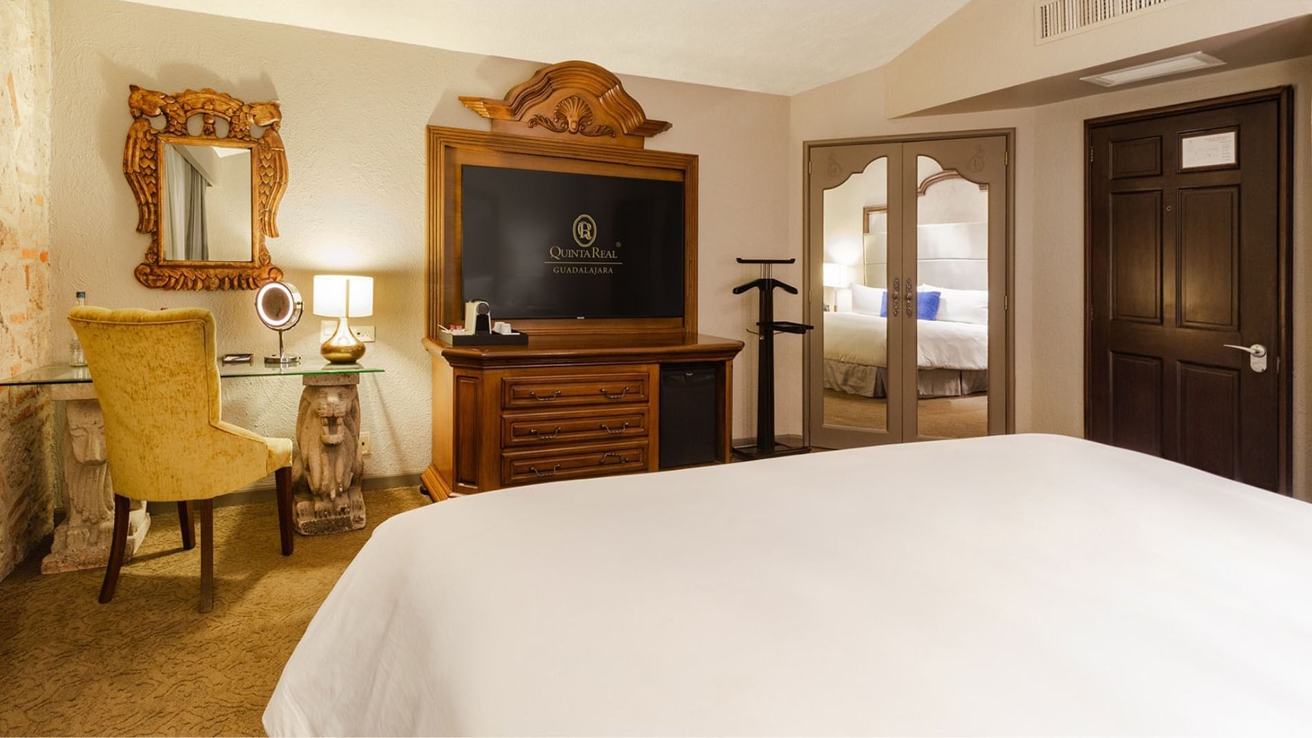 King Master Suite with a carved wooden TV console, mirror, and lion-base desk at Quinta Real Guadalajara