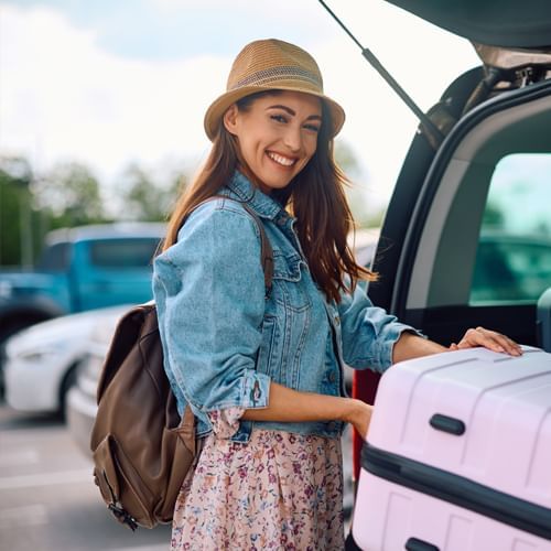 Woman stands beside her car, holding a suitcase at Rosen Inn Hotels and Resorts