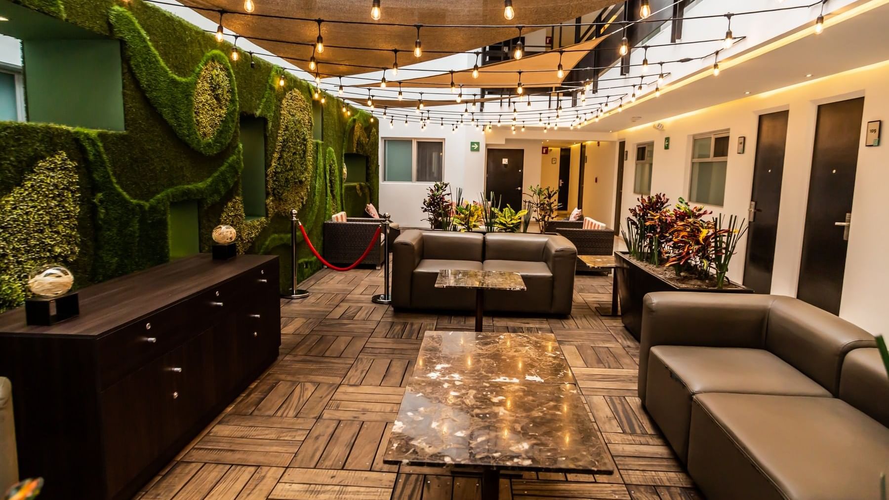 Illuminated lounge area with string lights, comfy sofas, coffee tables & indoor plants at Gamma Puebla Senorial Centro