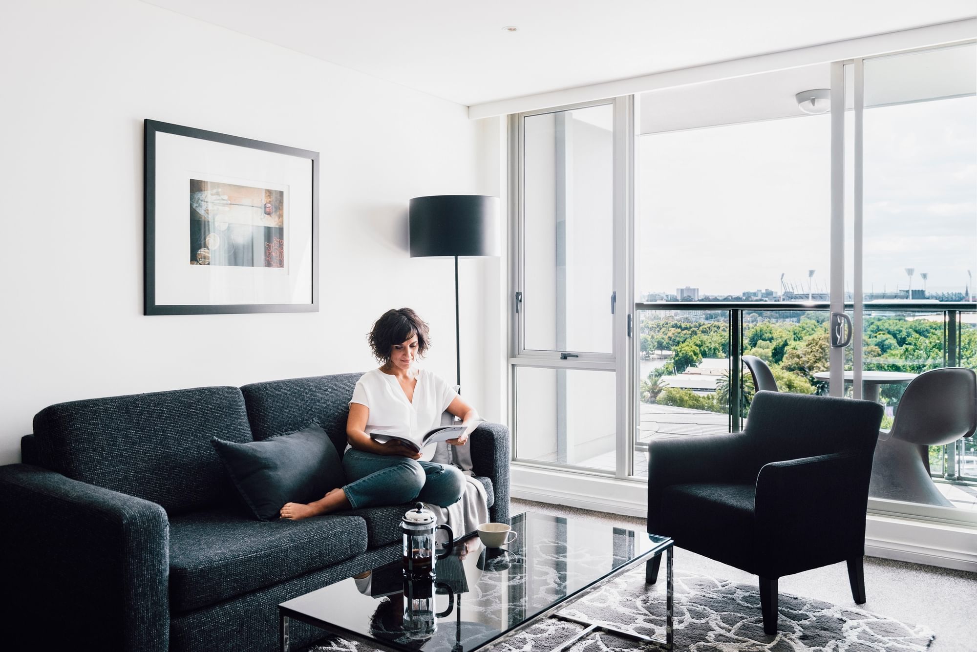 Lady reading on the couch in 1 Bedroom Deluxe Apartment at Quay West Suites Melbourne