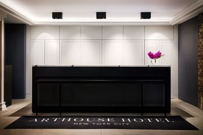 Arthouse Hotel New York City lobby with black reception desk, purple flowers, and black logo rug.