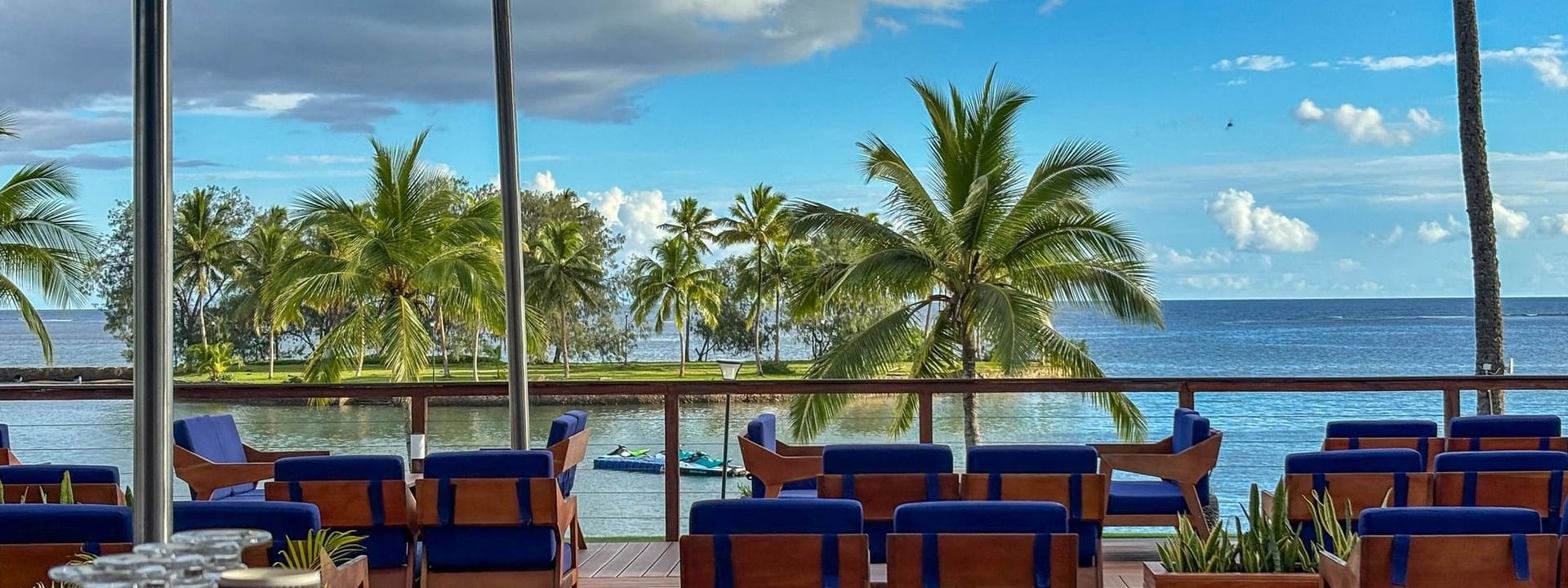 Blue armchairs on a wooden deck by coffee cups under a shade sail overlooking the ocean at The Naviti Resort in Korolevu