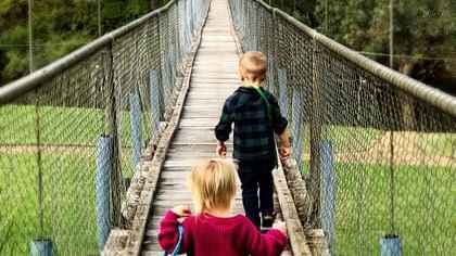 Boy and girl walk together across a wooden suspension bridge over a green field near The Sebel Mandurah