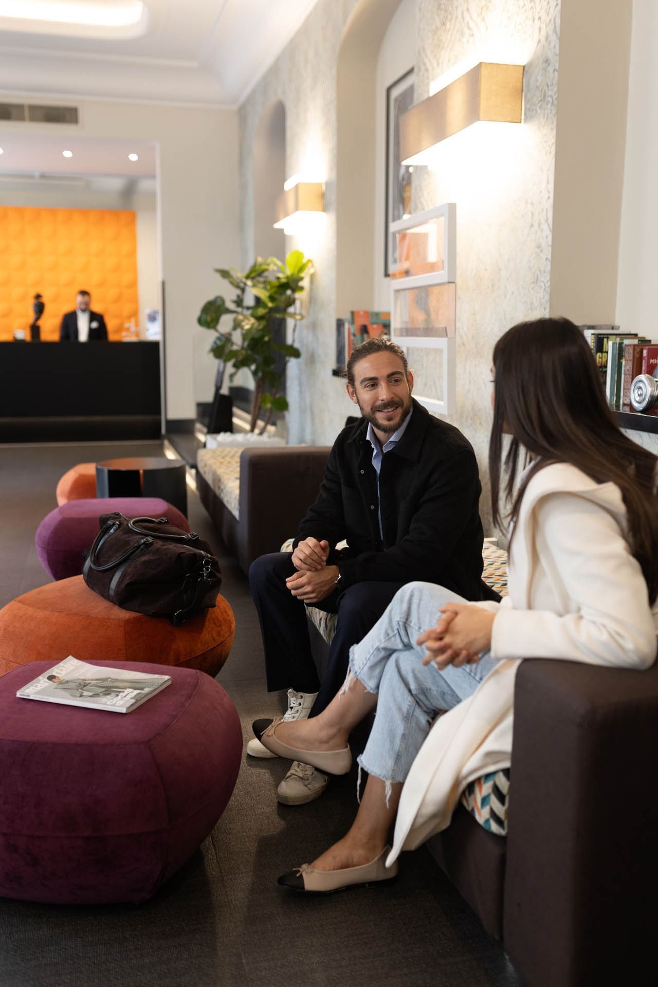 Woman in a white jacket chats with a man in a black jacket in a lobby, surrounded by colorful seating at The Republic Hotel