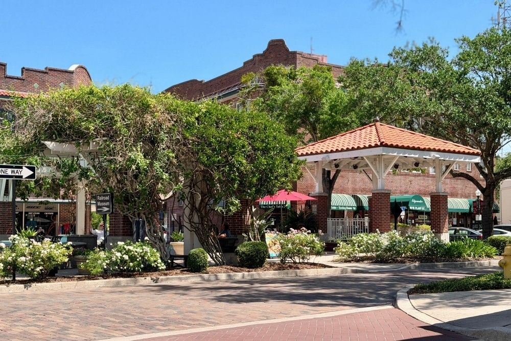 A red roofed pergola beside white trellises draped in green vines in the middle of a cobblestone street in Downtown Winter Garden.