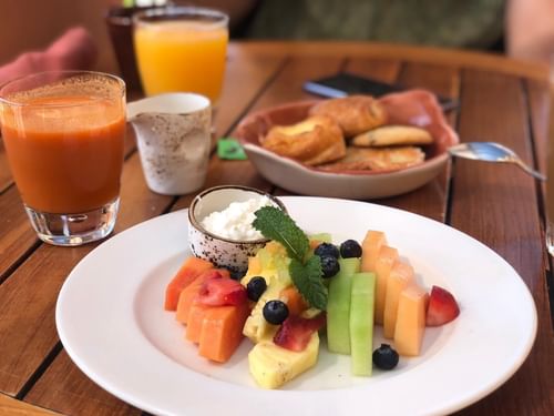 Fruta fresca, pasteles y jugo de naranja para desayunar en una mesa de madera en Tomates, Hacienda Del Mar, Los Cabos.
