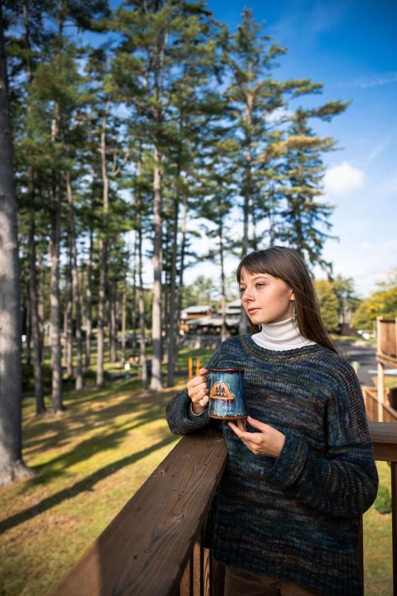 Person in a sweater holding a mug on a balcony in The Lodge at Schroon Lake