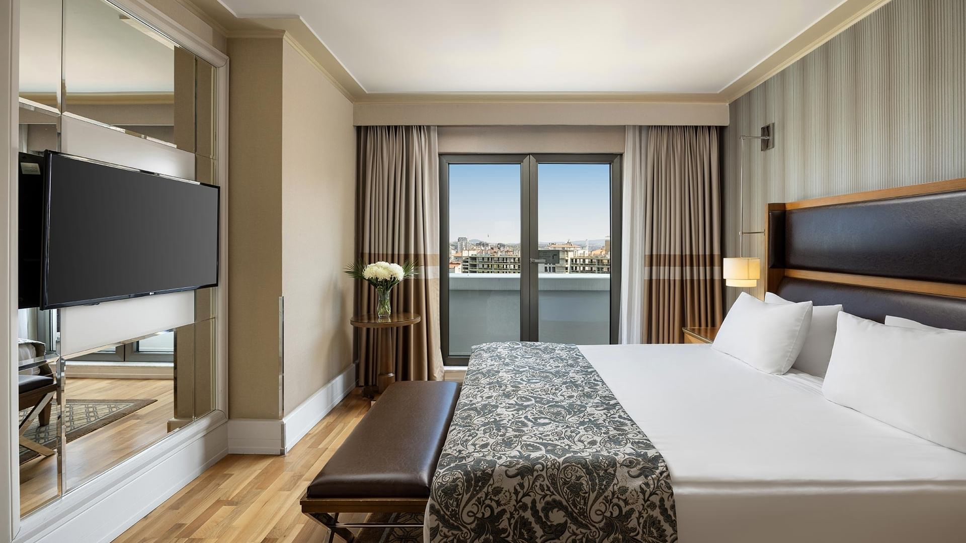 Titanic City Taksim's suite with a large bed, wooden floors, large windows, a television, and a large mirror.