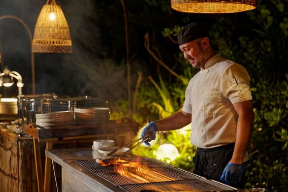 A chef in a traditional hat prepares food on a grill at Grand Park Kodhipparu, Maldives