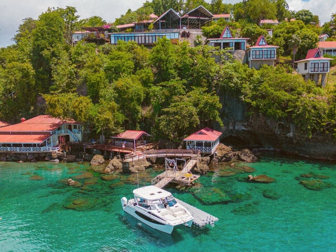 White catamaran anchored in turquoise waters near hillside resort with colorful villas and lush tropical vegetation