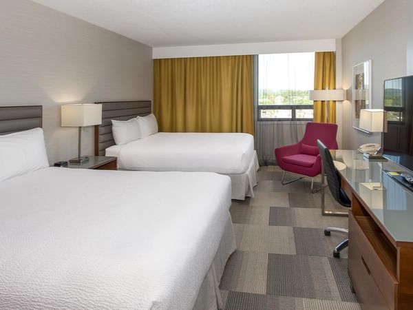 Spacious suite with, work desk, pink accent chair, and large window at Coast Prince George Hotel.