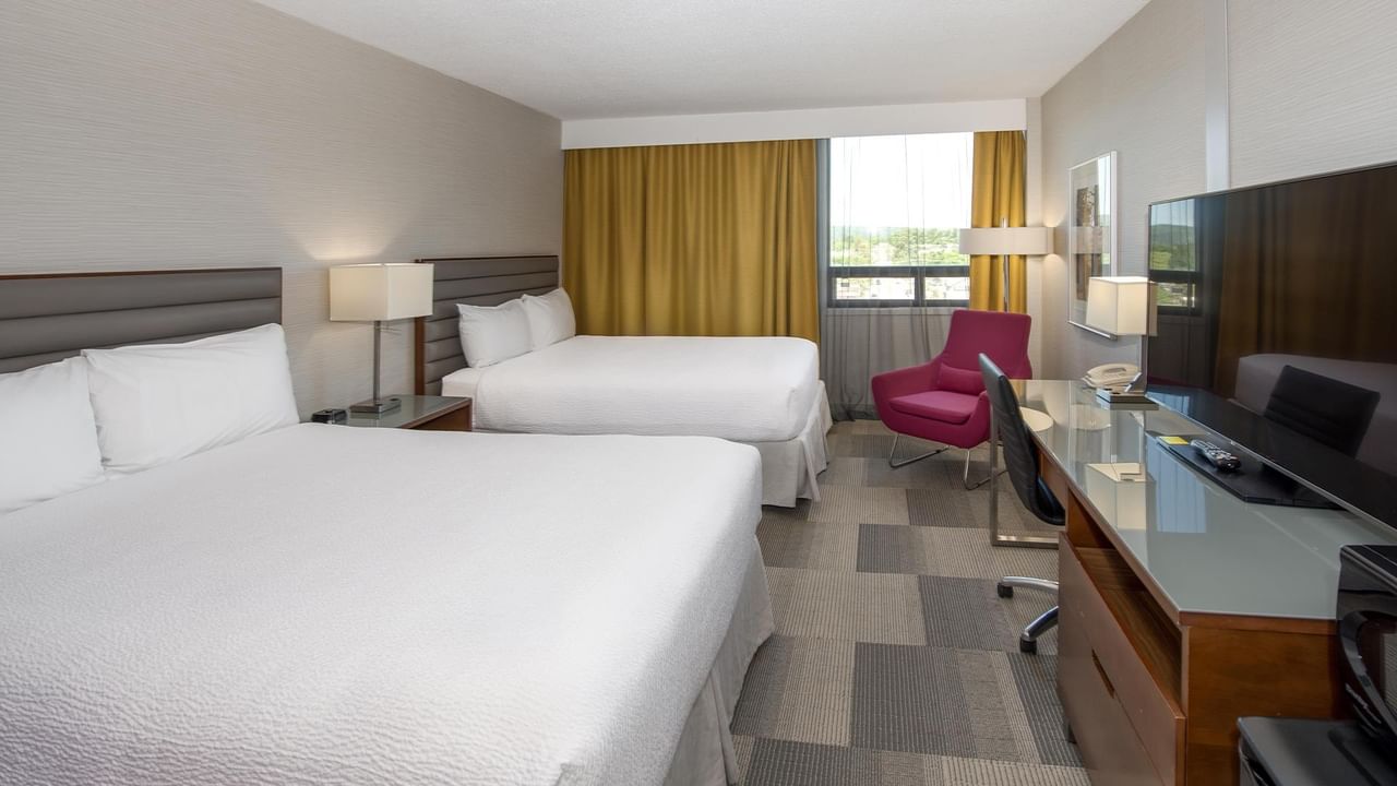 Spacious suite with, work desk, pink accent chair, and large window at Coast Prince George Hotel.