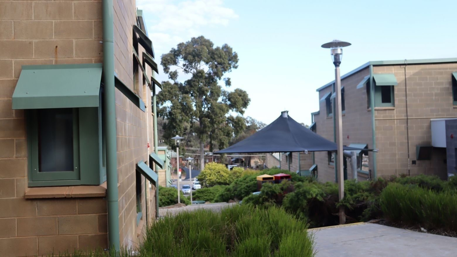 Green building exterior with a black canopy and greenery at La Trobe University.