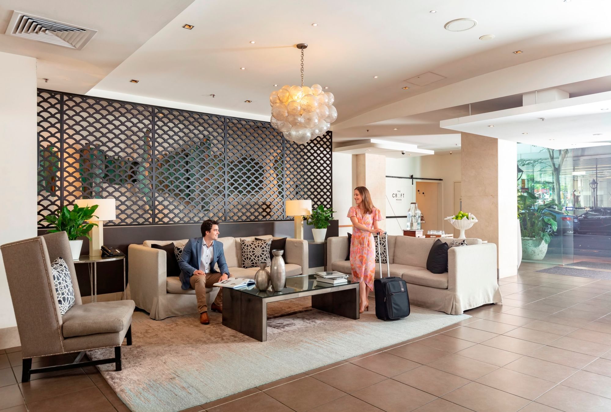 Guests relaxing in the stylish hotel lobby seating area with modern furniture and a bubble chandelier at The Sebel Brisbane