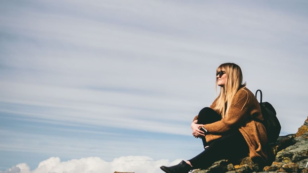 woman sitting on rocky ledge with vast sky in background