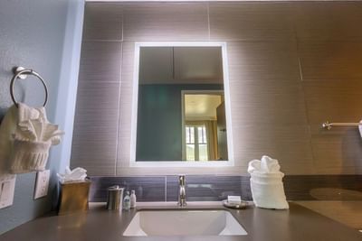 A modern bathroom with a white sink, a brightly lit mirror, and light wood-paneled walls in a room at The Stanley Hotel