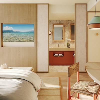 Modern hotel room with bed, TV, bathroom, and wooden table with chair.