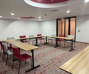 Mesas de reuniones en forma de U con sillas rojas y grises sobre alfombra estampada en Sala Fagua de Unika Hotels