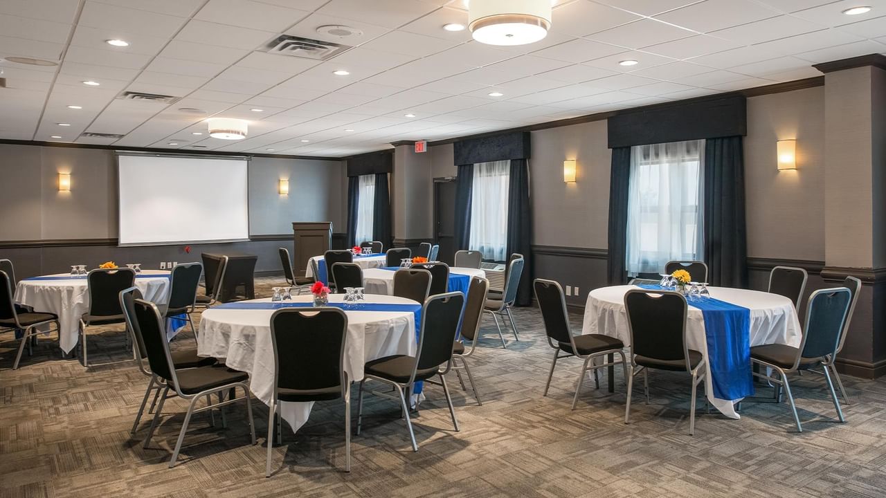 Meeting room with round tables, black chairs, and projection screen at Coast Calgary University Area Hotel by APA.