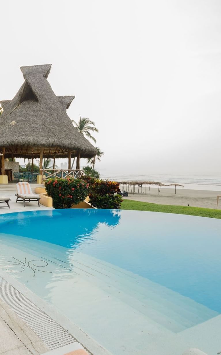 Infinity pool area with striped lounge chairs and white umbrellas near the beach shore at Quinta Real Acapulco