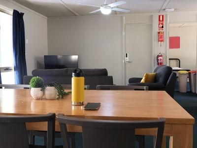 Wooden dining table with plants, a water bottle, and a smartphone on top in a living room at La Trobe University Villas.