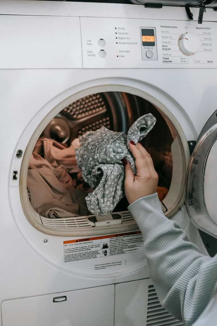 Close-up of a lady putting clothes in the laundry machine at Anaheim Portofino Inn & Suites