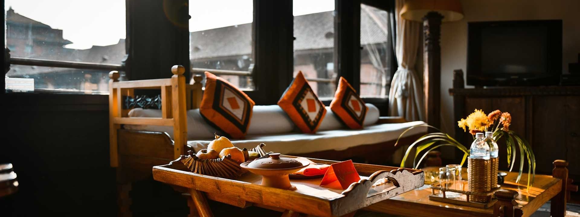 Parlor with sunlight streaming, featuring a wooden tray with snacks in Heritage Deluxe at The Dwarika’s Hotels and Resorts