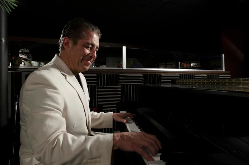 Smiling man in a white jacket playing a dark piano in a dimly lit room in Chandler's Steakhouse at Hotel 43 Boise