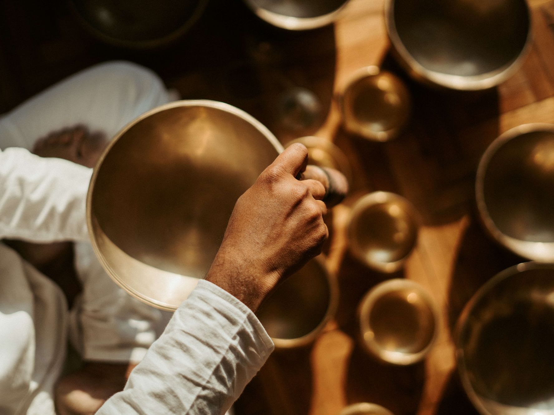 Hand holding a brass bowl above a collection of various brass bowls on a wooden floor at Dwarika's Himalayan Wellbeing