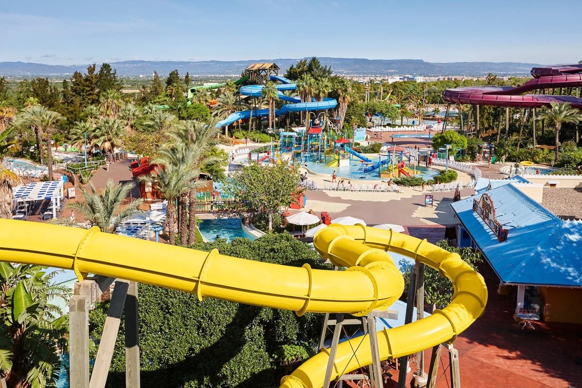 High-angle shot of a vibrant water park featuring a winding yellow slide in the foreground and blue slides in the background.
