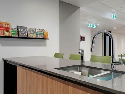Modern communal kitchen with stainless steel sink, cookbooks on shelf, and green seating area at UniLodge Auckland Central