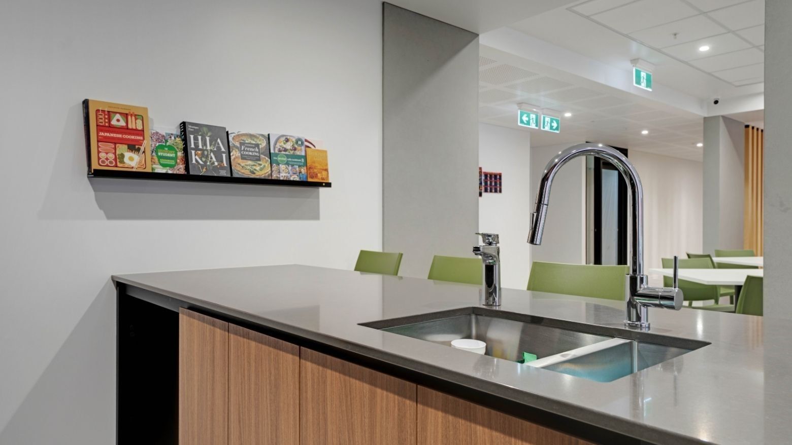 Modern communal kitchen with stainless steel sink, cookbooks on shelf, and green seating area at UniLodge Auckland Central