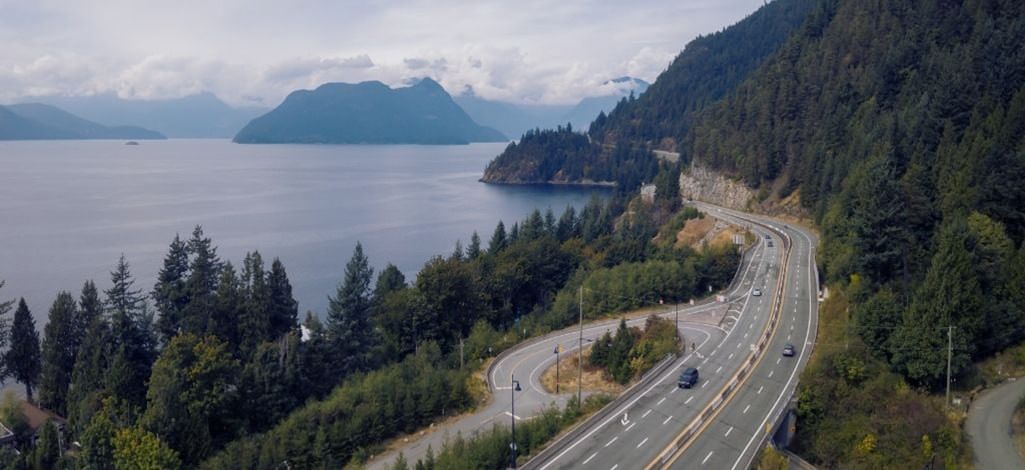 A winding stretch of the Sea to Sky Highway surrounded by lush forests with Howe Sound’s calm waters in the background.