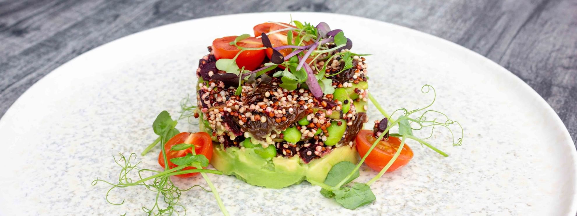 A dish with quinoa, green beans, and avocado on a white plate with garnishes and a wooden surface.