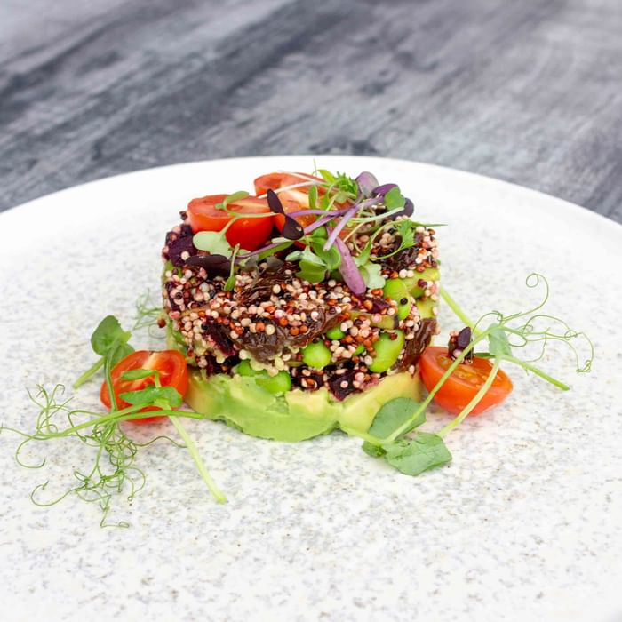 Plate with quinoa, avocado, green beans, and tomatoes garnished with herbs, served on a wooden table.