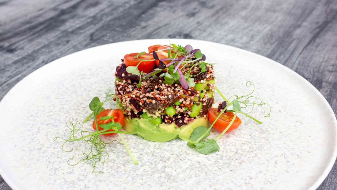 A dish with quinoa, green beans, and avocado on a white plate with garnishes and a wooden surface.