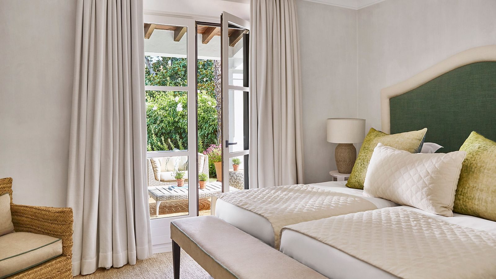 Four-bedroom villa featuring twin beds and a cushioned bench facing a patio with seating at Marbella Club