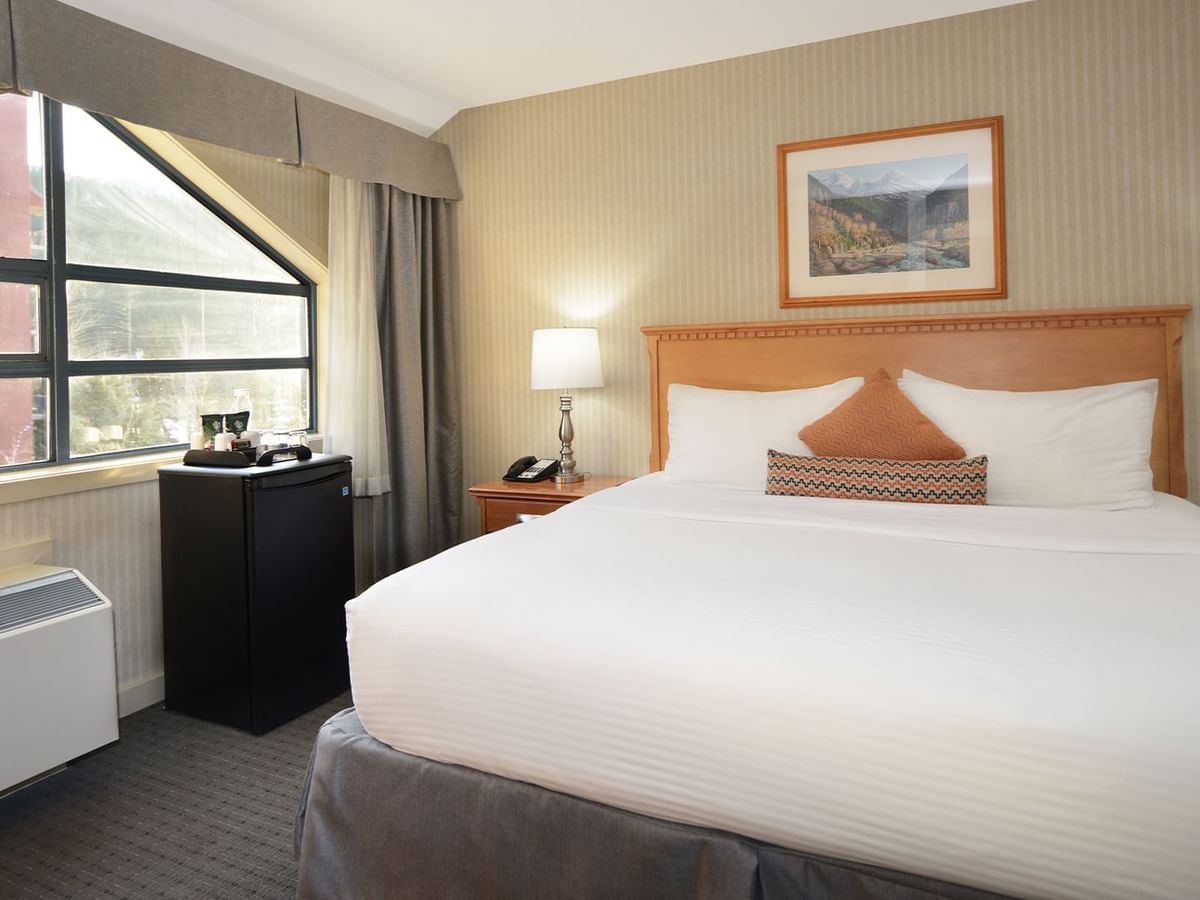 Spacious hotel room with a king bed, elegant decor and large window for natural light.