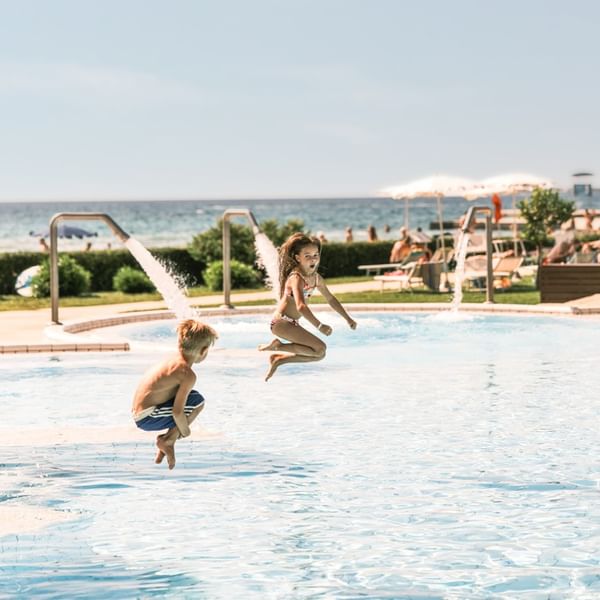 Bambini che saltano in piscina vicino al mare presso Falkensteiner Group