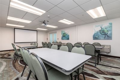 Modern meeting room with table set-up, projector screen, and carpeted floors at Off Shore Resort
