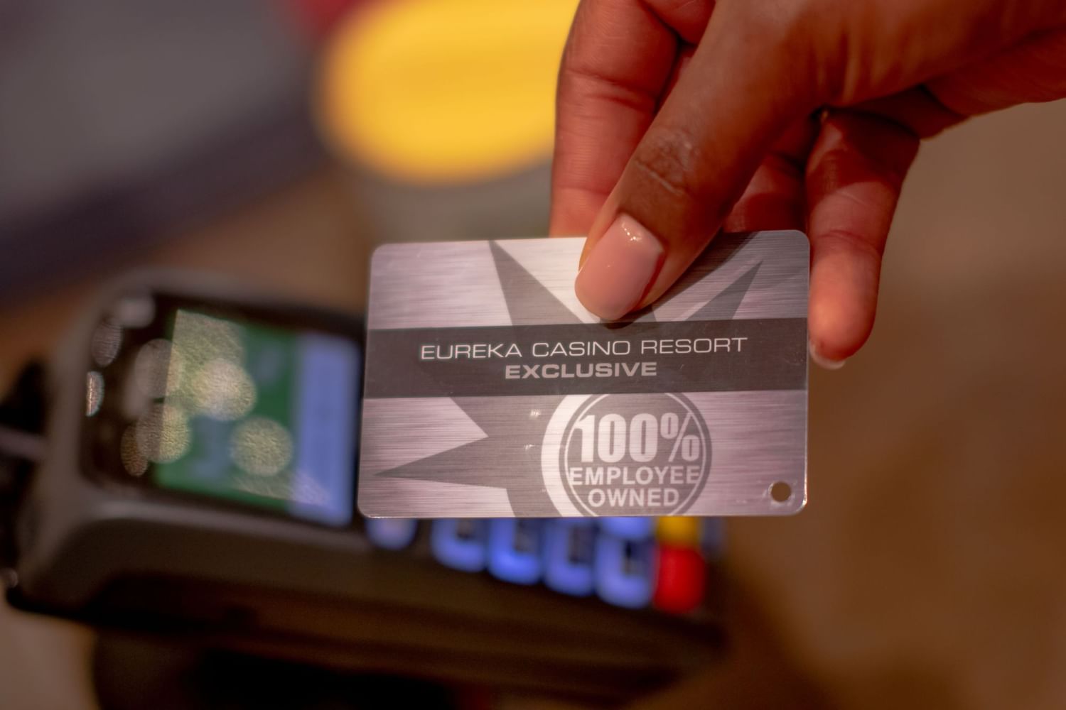 Hand holding silver employee-owned membership card over payment terminal inside casino area at Eureka Casino Resort