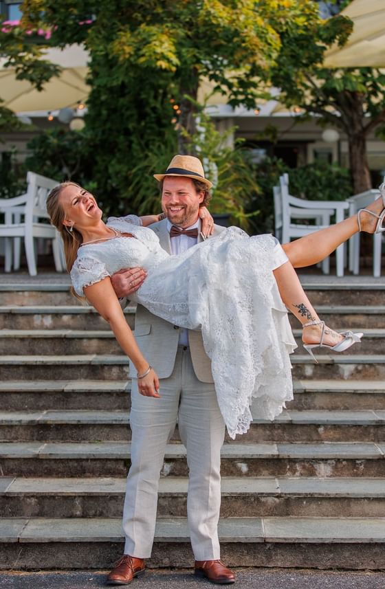Joyful groom lifts laughing bride on stone steps outside the beautiful Tyrifjord Hotel in Norway