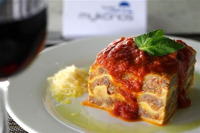 A piece of delicious lasagna with red sauce and basil, next to a glass of wine at Hotel Mykonos